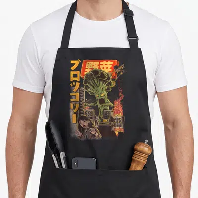 Tablier de cuisine noir avec illustration d'un monstre brocoli détruisant une ville japonaise et une femme effarée.