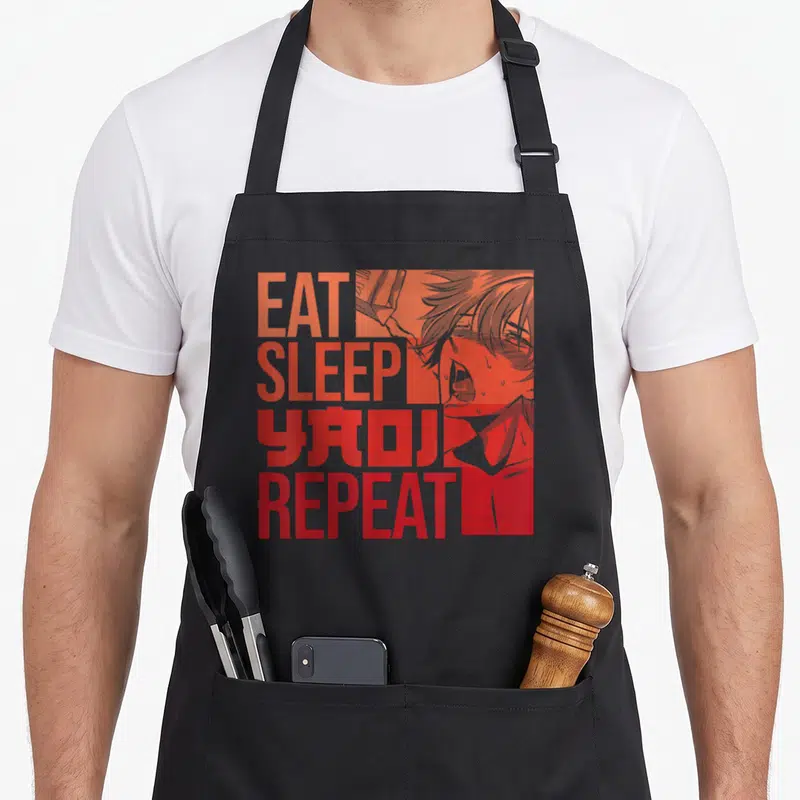 Tablier de cuisine noir avec inscription EAT SLEEP YAOI REPEAT et dessin de personnage manga en teintes orangées.