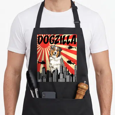 Tablier de cuisine noir avec illustration Dogzilla Berger Australien géant au-dessus d'une ville et d'hélicoptères sur fond de soleil levant.