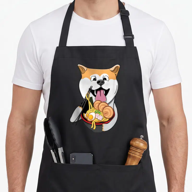 Tablier de cuisine noir avec illustration d'un chien Akita Inu mangeant du ramen avec des baguettes.