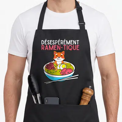 Tablier de cuisine noir avec illustration d'un Shiba Inu dans un bol de ramen et le texte Désespérément Ramen-tique en haut.