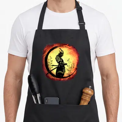 Tablier de cuisine noir avec illustration d'un samouraï Yasuke tenant une katana devant un soleil orange.