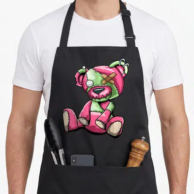 Tablier de cuisine noir avec illustration d'un ourson rose et vert aux coutures apparentes et au bandage sur l'œil.