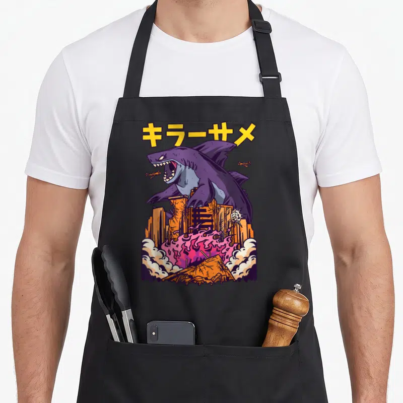 Tablier de cuisine noir avec un grand shark violet détruisant des bâtiments orange et des avions.