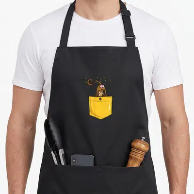 Tablier de cuisine noir avec un singe kawaii sortant d'une poche jaune suspendue à une branche.