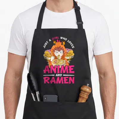 Tablier de cuisine noir avec une illustration kawaii d'une fille en costume de crabe mangeant un bol de ramen entourée de bols géants.