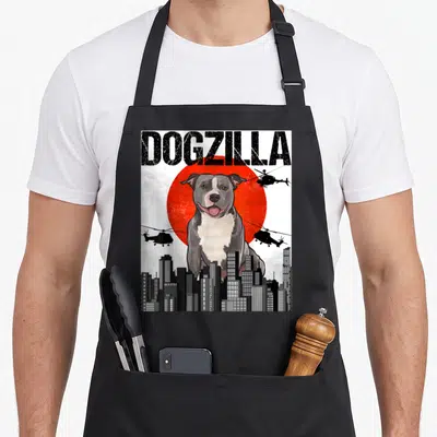 Tablier de cuisine noir avec illustration d'un chien géant nommé Dogzilla dominant une ville et des hélicoptères.