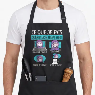 Tablier de cuisine noir avec une illustration d'une fille en pull devant un laptop et des textes sur l'anime.