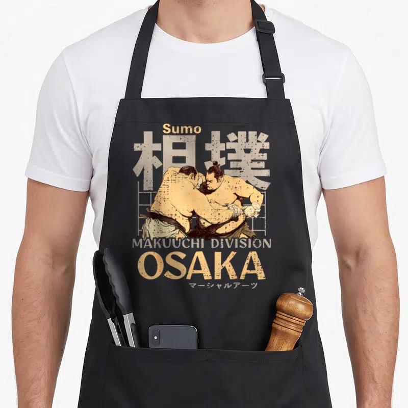 Tablier de cuisine noir avec illustration vintage de deux lutteurs de sumo et le mot Osaka en lettres capitales jaunes.