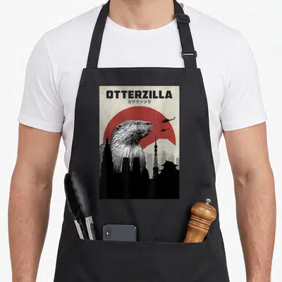 Tablier de cuisine noir avec illustration d'un loutre géant OTTERZILLA devant Tokyo et un soleil rouge.
