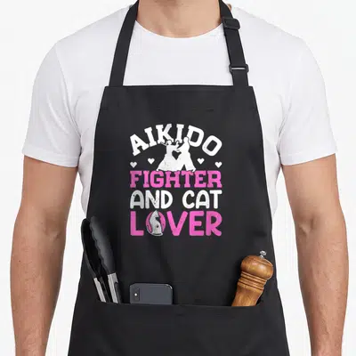 Tablier de cuisine noir avec l'inscription Aikido Fighter and Amoureux de Chat en blanc et rose, incluant une silhouette de chat dans la lettre O.