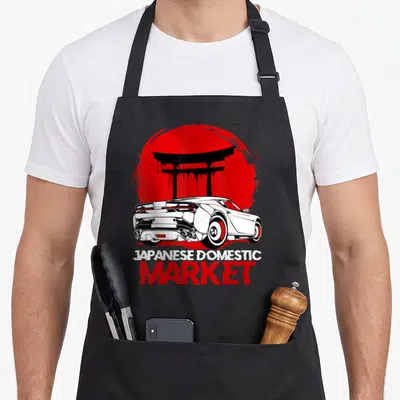 Tablier de cuisine noir avec illustration voiture blanche, portail torii rouge et texte Japanese Domestic Market.