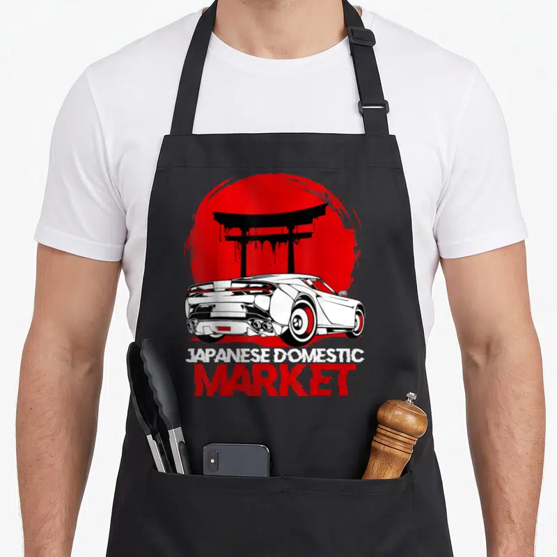 Tablier de cuisine noir avec illustration voiture blanche, portail torii rouge et texte Japanese Domestic Market.