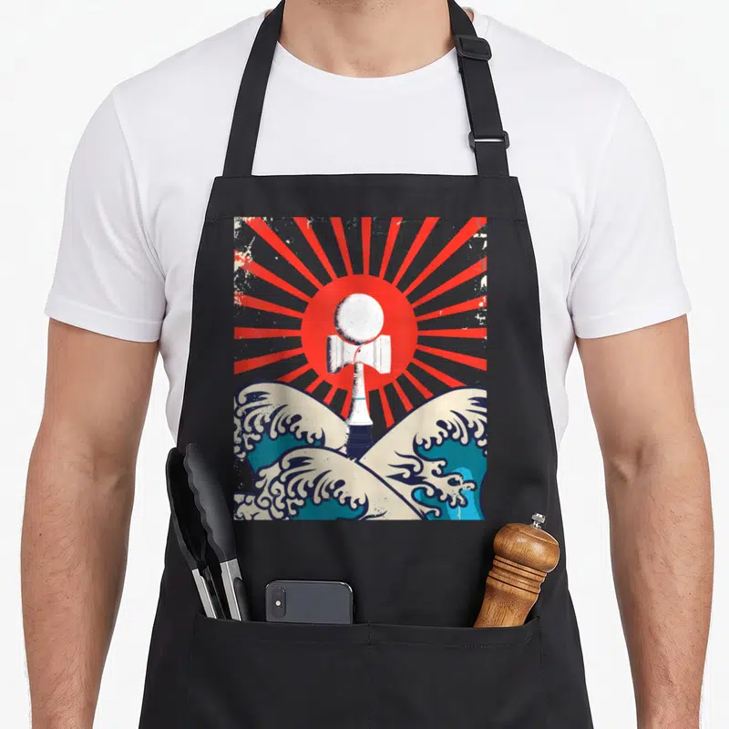 Tablier de cuisine noir avec illustration d'un kendama blanc sur des vagues bleues et un soleil rouge à rayons.