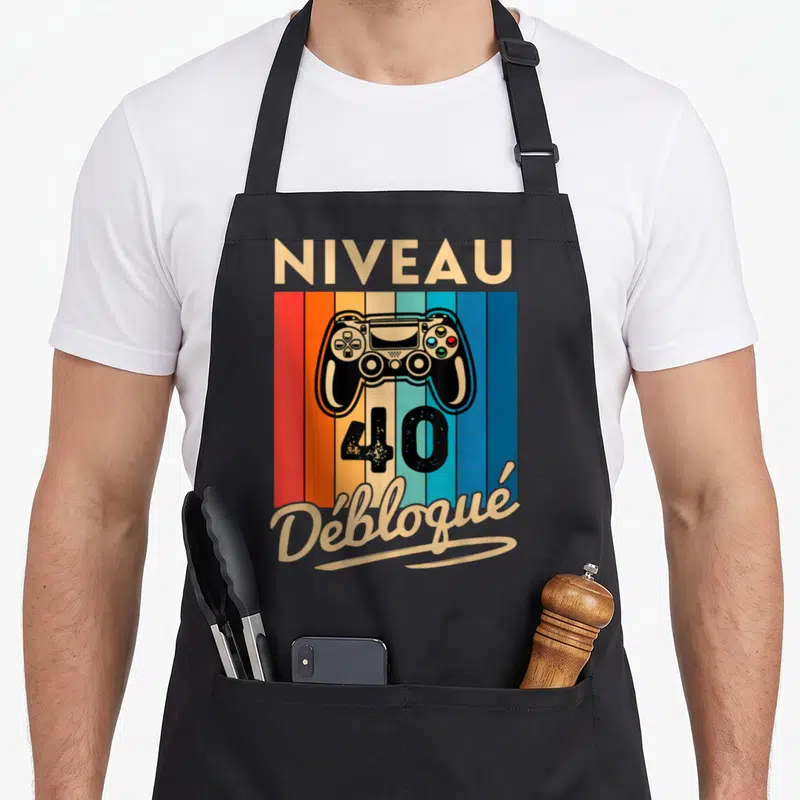 Tablier de cuisine noir avec manette de jeu et texte Niveau 40 Débloqué sur fond coloré