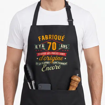 Tablier de cuisine noir avec inscription vintage orange et rouge célébrant les 70 ans avec une blague sur les pièces d'origine.