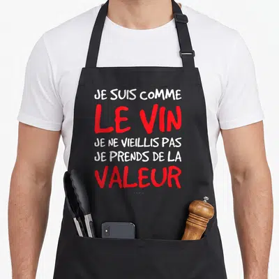 Tablier de cuisine noir avec une citation humoristique en lettres blanches et rouges sur fond uni.