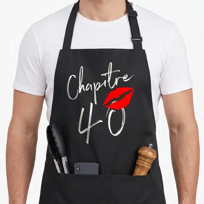 Tablier de cuisine noir avec inscription Chapitre 40 et empreinte de rouge à lèvres rouge vif sur fond uni.