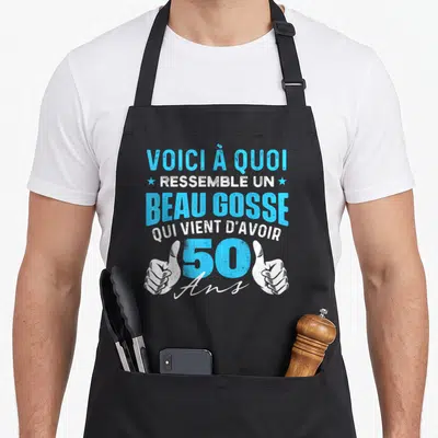 Tablier de cuisine noir avec inscription bleu et blanc célébrant les cinquante ans avec deux pouces levés.