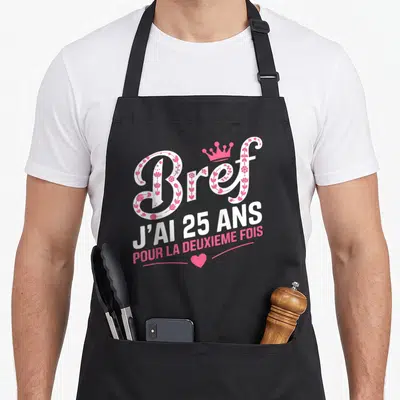 Tablier de cuisine noir avec l'inscription Bref j'ai 25 ans pour la deuxième fois en blanc et rose orné d'une couronne.