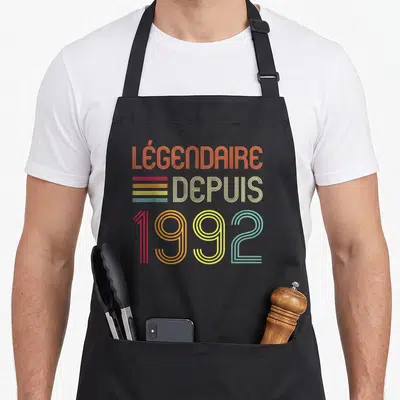 Tablier de cuisine noir avec inscription Légendaire Depuis 1992 en lettres colorées style rétro.