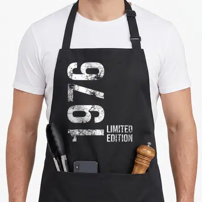 Tablier de cuisine noir avec inscription 1976 Limited Edition en typographie blanche verticalement alignée sur le devant.