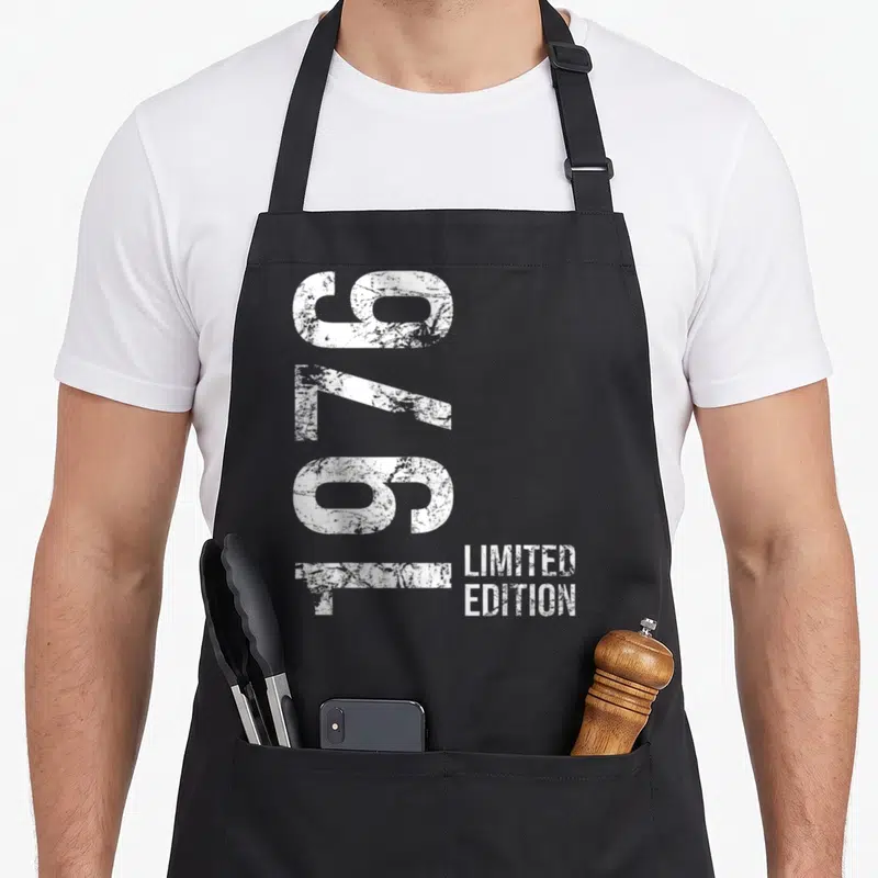 Tablier de cuisine noir avec inscription 1976 Limited Edition en typographie blanche verticalement alignée sur le devant.