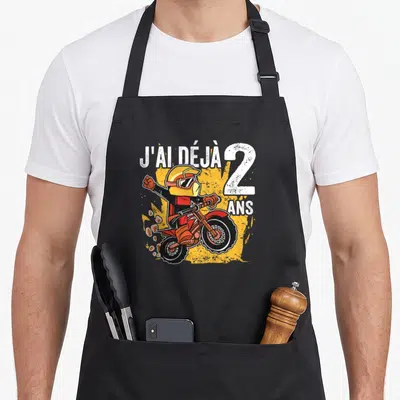 Tablier de cuisine noir avec un petit motard et l'inscription J'ai déjà 2 ans en blanc sur fond jaune.