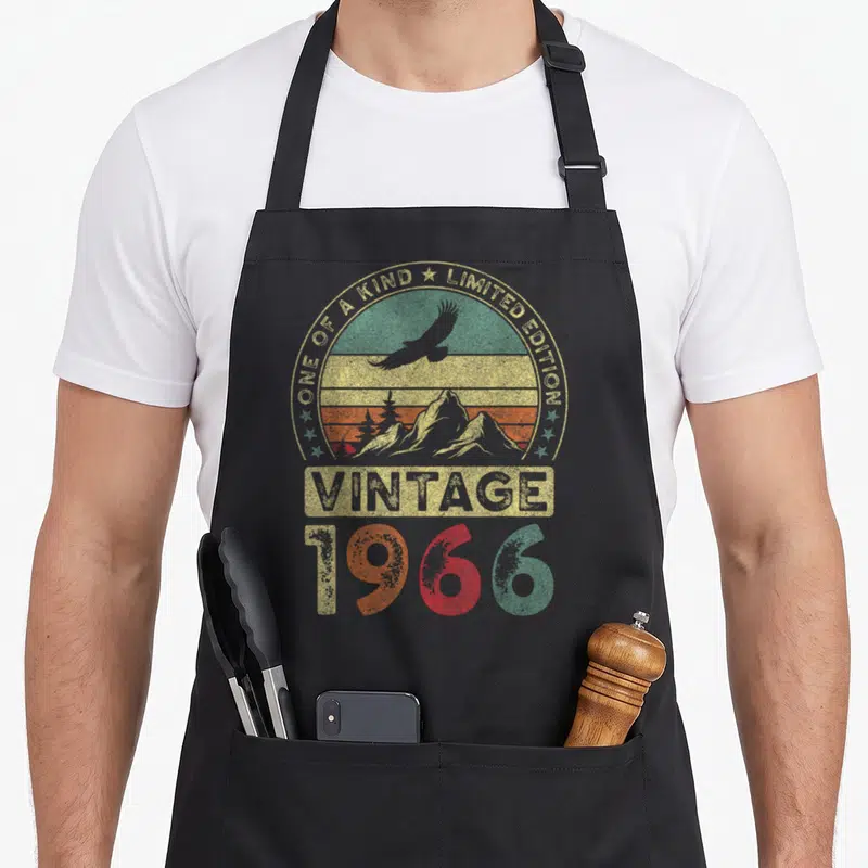 Tablier de cuisine noir avec illustration vintage montrant des montagnes, un aigle et l'année 1966 en couleurs dégradées.