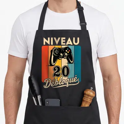 Tablier de cuisine noir avec manette de jeu vidéo et texte Niveau 20 Débloqué sur fond coloré vintage.