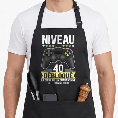 Tablier de cuisine noir avec illustration de manette de jeu vidéo et texte Niveau 40 Débloqué en blanc et jaune.