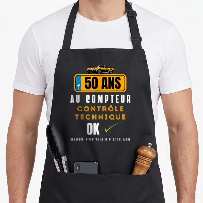 Tablier de cuisine noir avec illustration plaque 50 ans au compteur contrôle technique OK et voiture jaune vintage.