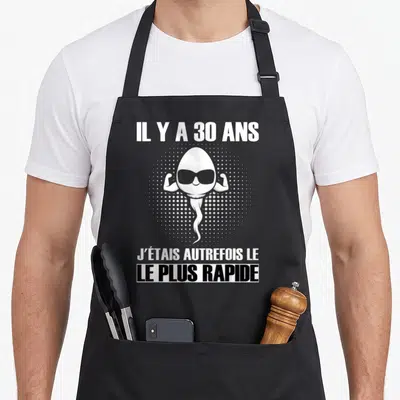 Tablier de cuisine noir avec un spermatozoïde musclé aux lunettes noires et texte blanc.