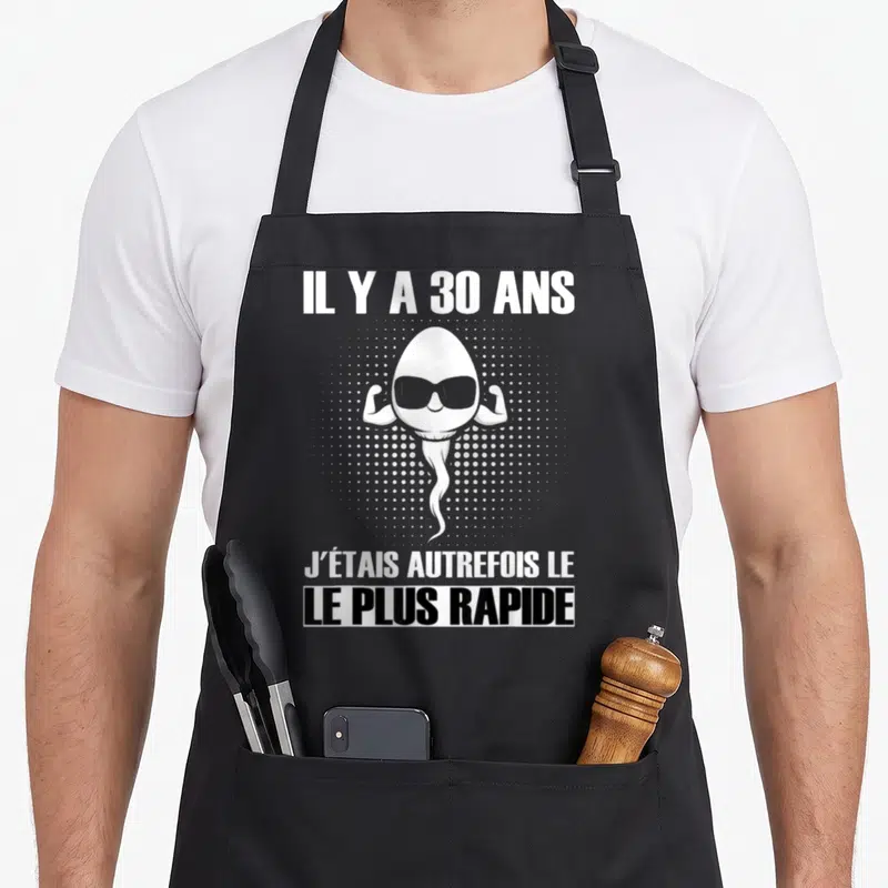 Tablier de cuisine noir avec un spermatozoïde musclé aux lunettes noires et texte blanc.