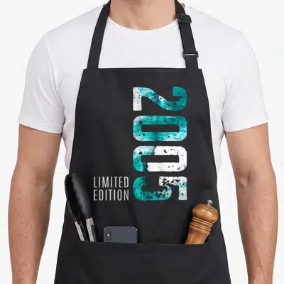 Tablier de cuisine noir avec chiffres 2005 remplis de motifs marins turquoise et texte limited edition en bas à gauche.