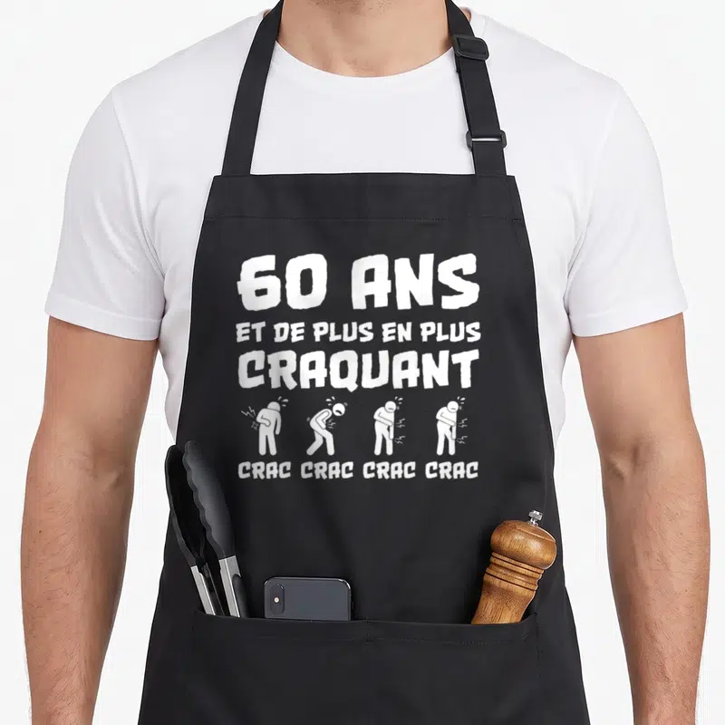 Tablier de cuisine noir avec texte 60 ans et de plus en plus craquant et silhouettes blanches illustrant des articulations qui grincent.