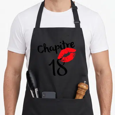 Tablier de cuisine noir avec inscription Chapitre 18 et empreinte de lèvres rouges stylisée au centre du design.