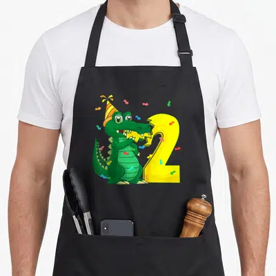 Tablier de cuisine noir avec un crocodile vert festif mordant un chiffre 2 jaune et des confettis.