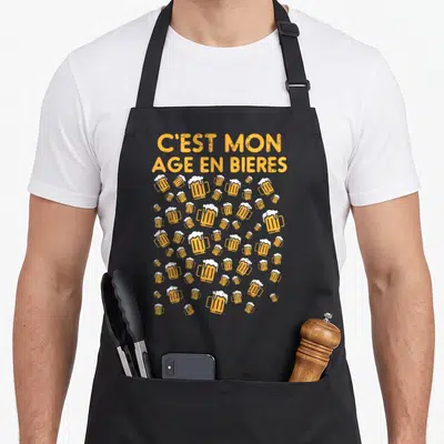 Tablier de cuisine noir avec inscription C'est mon âge en bières et motifs de verres de bière orange.