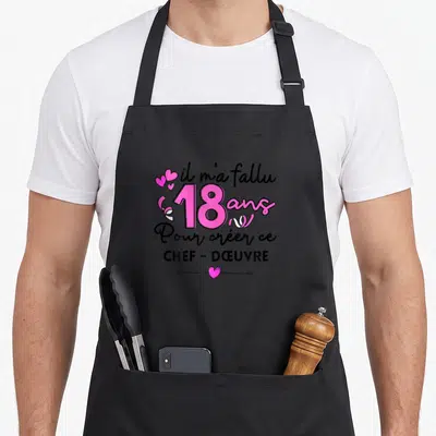 Tablier de cuisine noir avec l'inscription Il m'a fallu 18 ans pour créer ce chef-dœuvre en rose et noir.