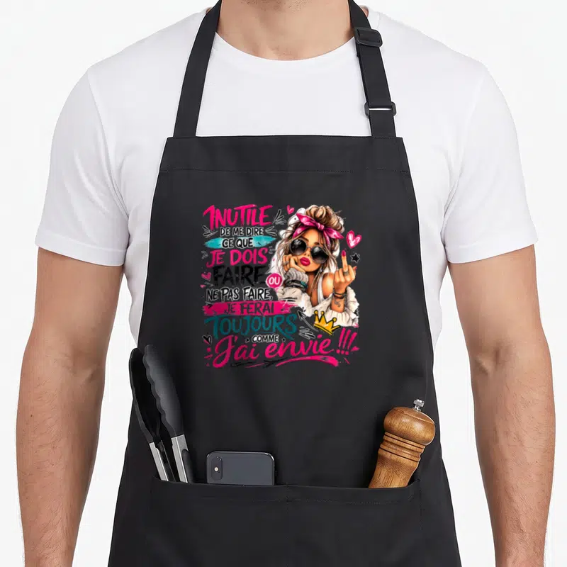 Tablier de cuisine noir avec illustration d'une femme coquette au doigt d'honneur et texte humoristique rose et bleu.