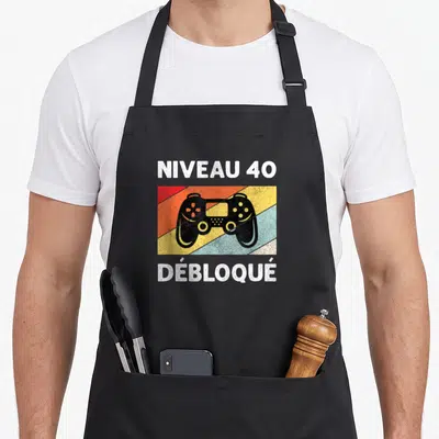 Tablier de cuisine noir avec illustration manette et texte Niveau 40 Débloqué sur fond rayé coloré.