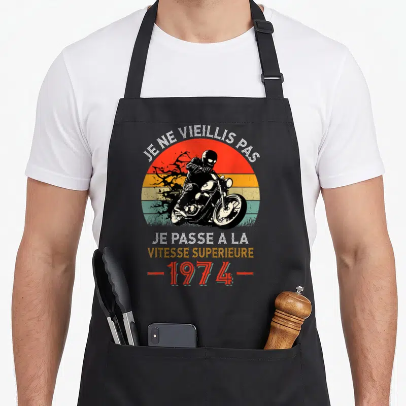 Tablier de cuisine noir avec un motard stylisé et le texte Je ne vieillis pas sur fond de soleil couchant multicolore.
