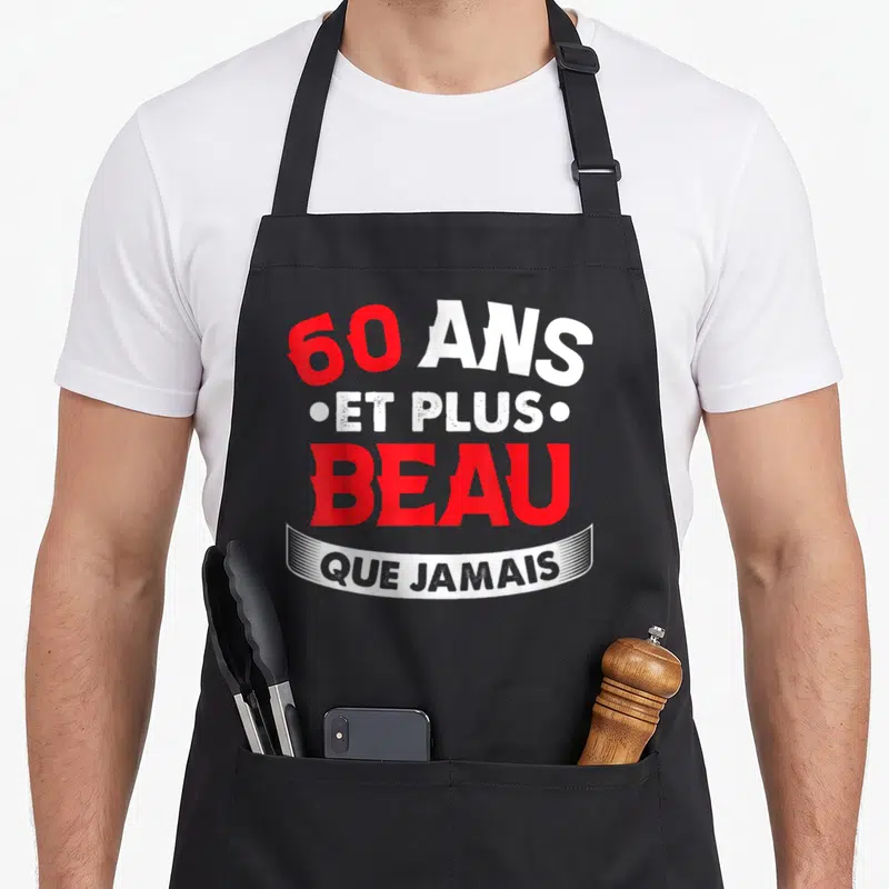 Tablier de cuisine noir avec l'inscription 60 ans et plus beau que jamais en typographie rouge et blanche.