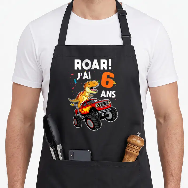 Tablier de cuisine noir avec un dinosaure orange sur un monster truck rouge et l'inscription Roar J'ai 6 Ans.