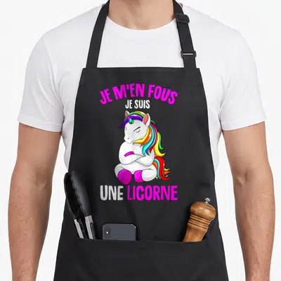 Tablier de cuisine noir avec une licorne blanche aux bras croisés et texte rose vif