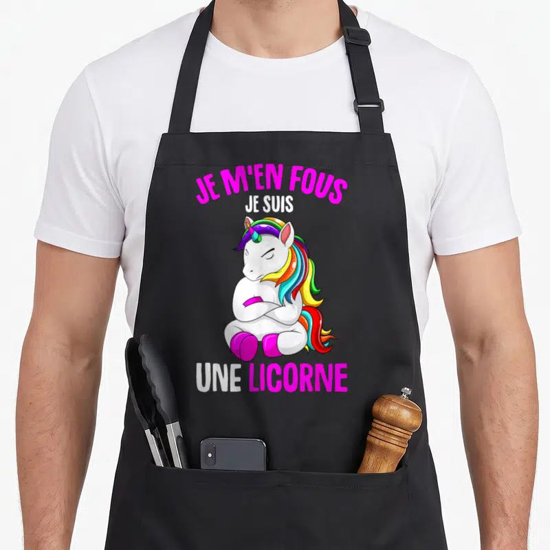 Tablier de cuisine noir avec une licorne blanche aux bras croisés et texte rose vif