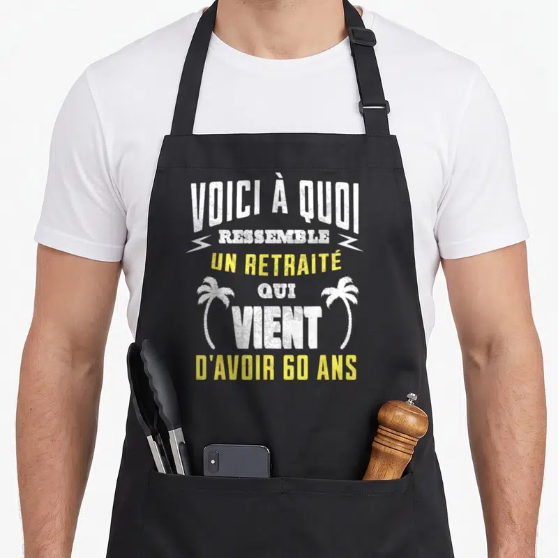 Tablier de cuisine noir avec le texte Voici à quoi ressemble un retraité qui vient d'avoir 60 ans encadré par deux palmiers blancs et jaunes.