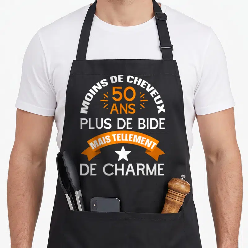 Tablier de cuisine noir avec inscription Moins de cheveux plus de bide mais tellement de charme en orange et blanc.