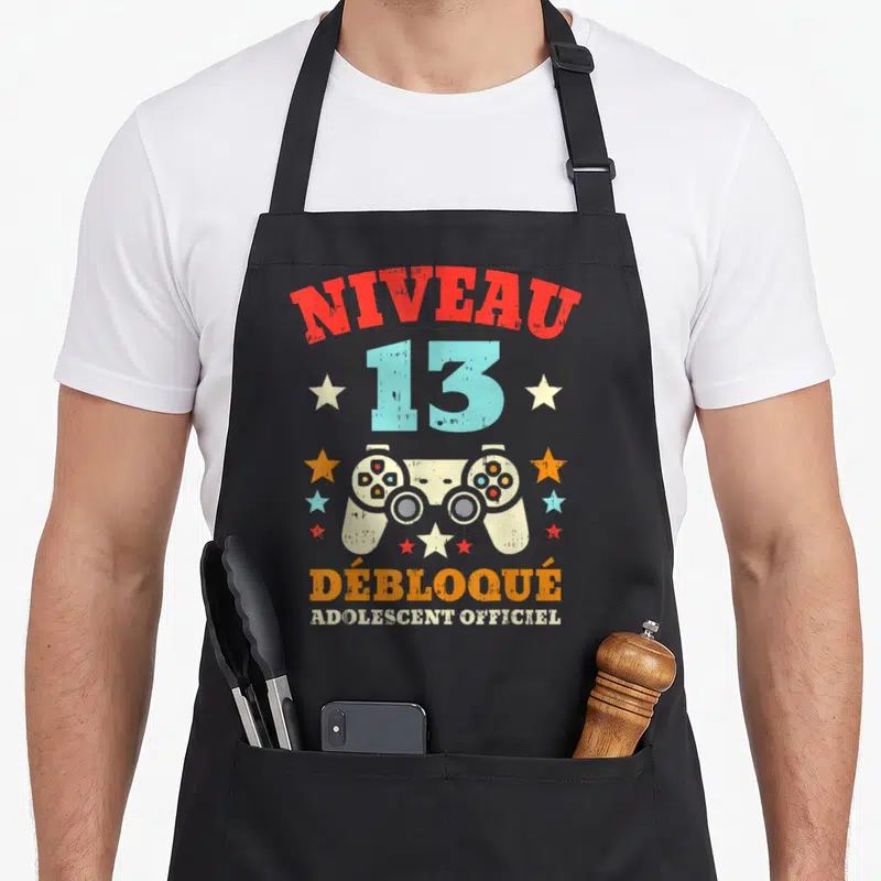 Tablier de cuisine noir avec inscription Niveau 13 Débloqué Adolescent et illustration de manette de jeu vidéo vintage.